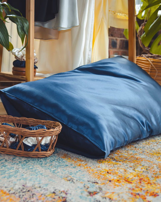 Navy 100% pure silk pillowcase with a wicker basket and colorful rug in the foreground